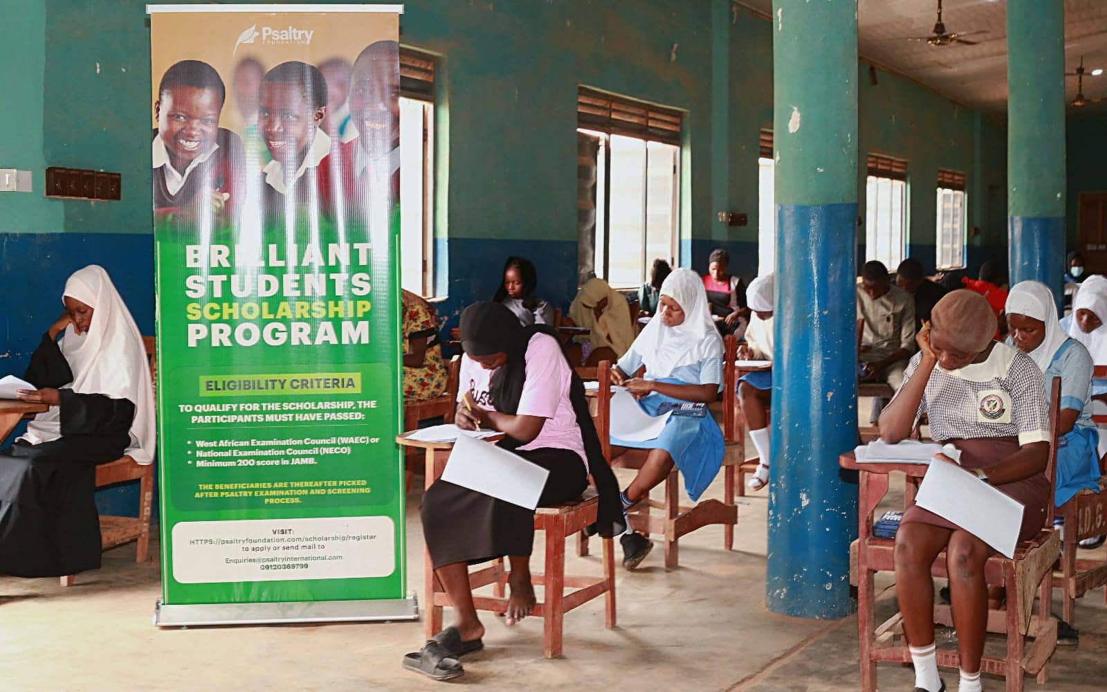 Applicants writing the Brilliant Students' Scholarship screening test beside a Psaltry Foundation banner